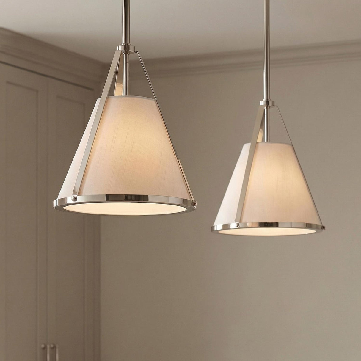 A transitional kitchen features two Hoyt Small Conical Pendant 9-inch Polished Nickel fixtures with linen shades hanging over the island alongside taupe cabinetry and recessed wall panels.