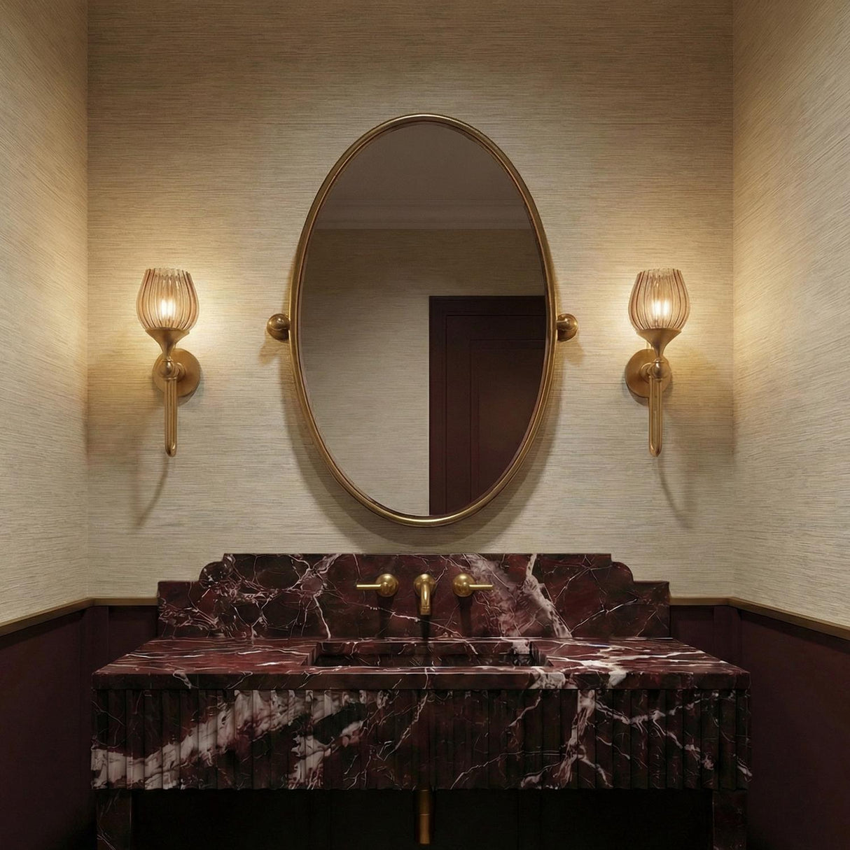A traditional bathroom with two Octavia Wall Sconces in aged brass and smoke taupe ribbed glass flanking an oval mirror above a burgundy marble vanity.