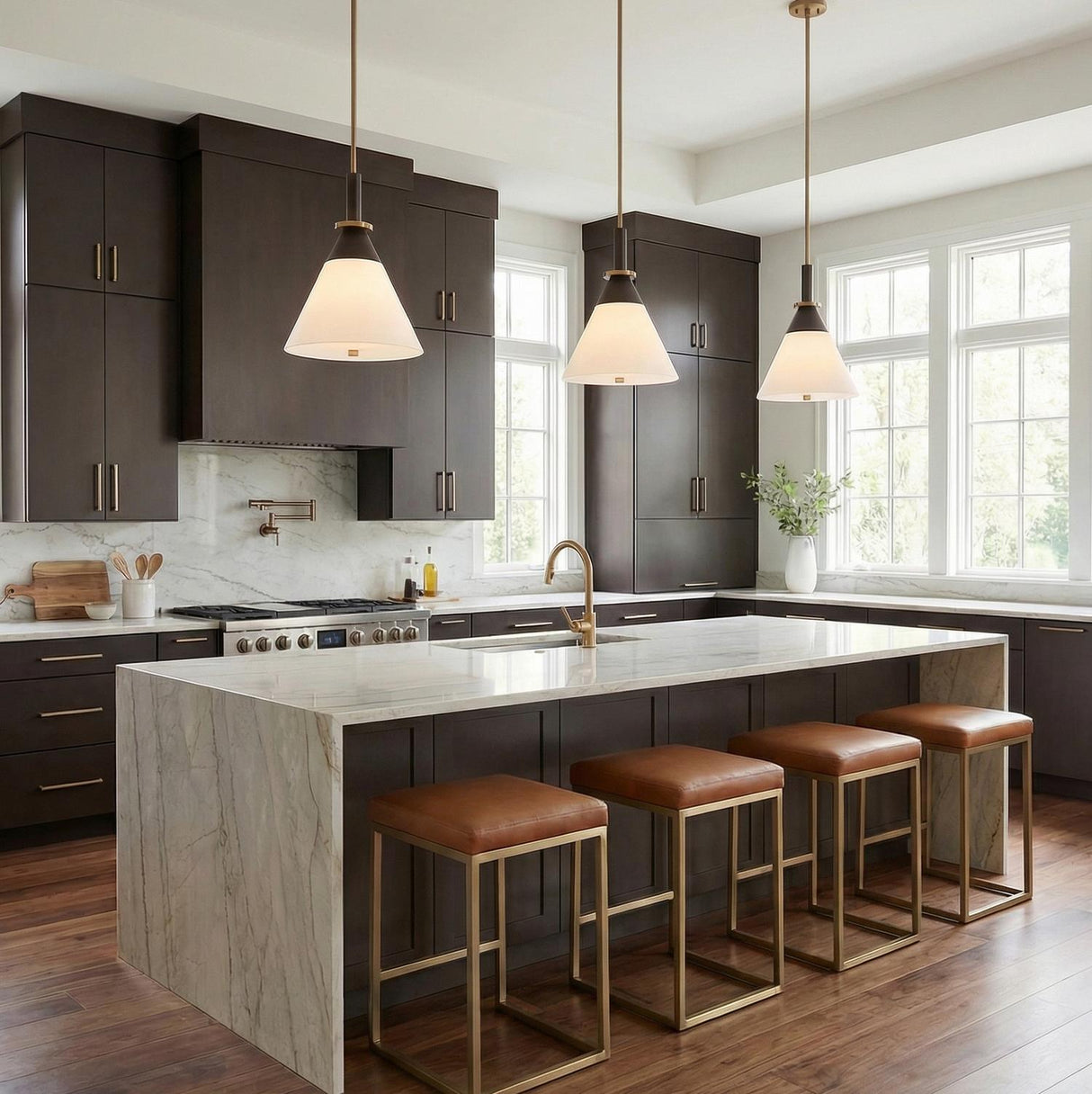 A transitional kitchen features three Armon Medium Pendant 16", Opal Glass with Bronze and Patina Brass fixtures suspended over a white marble waterfall island and dark cabinetry.