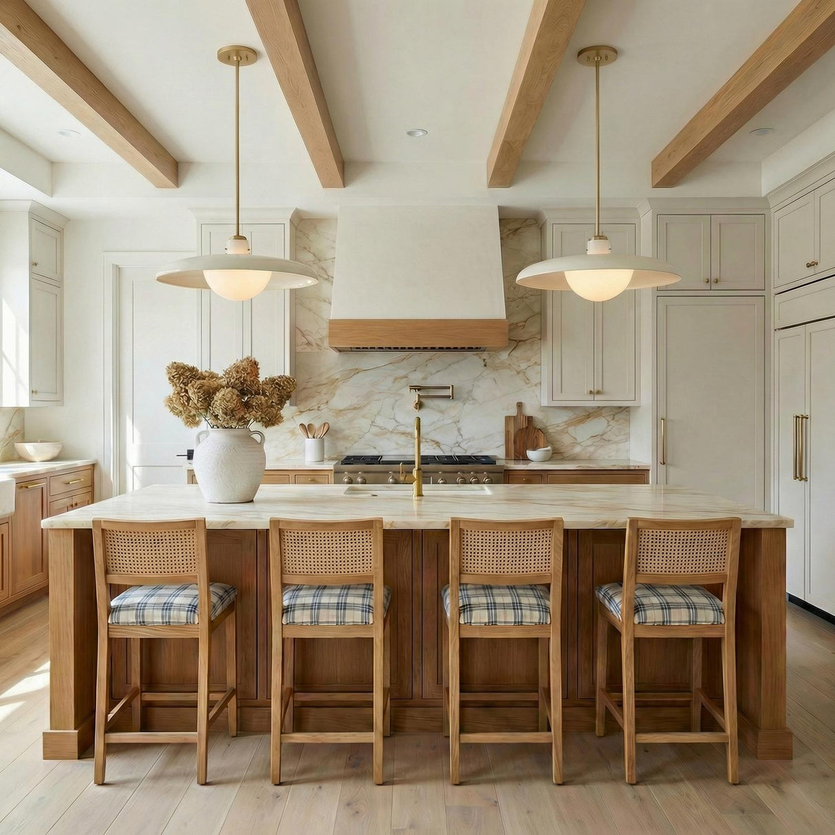 A transitional kitchen features two Bain Extra Large Pendant 28", Off-White and Patina Brass over the marble island under a beamed ceiling with rattan bar stools.