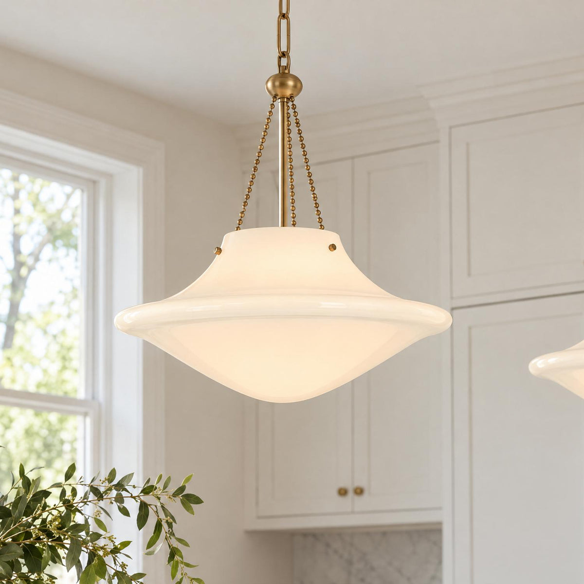 A transitional kitchen features the Balina Large Pendant 18", Patina Brass and Milk Glass hanging near white shaker cabinets and a window.