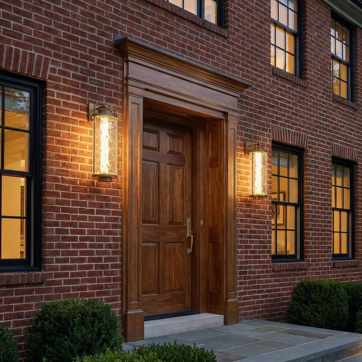 A traditional outdoor entryway with two Catalina LED Outdoor Wall Lights in patina brass and textured glass flanking a wood front door on a red brick facade.