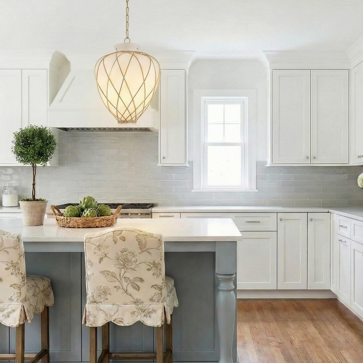 Natural rattan woven geometric pendant in a Cottage Kitchen with floral slipcovered stools and a white marble island.