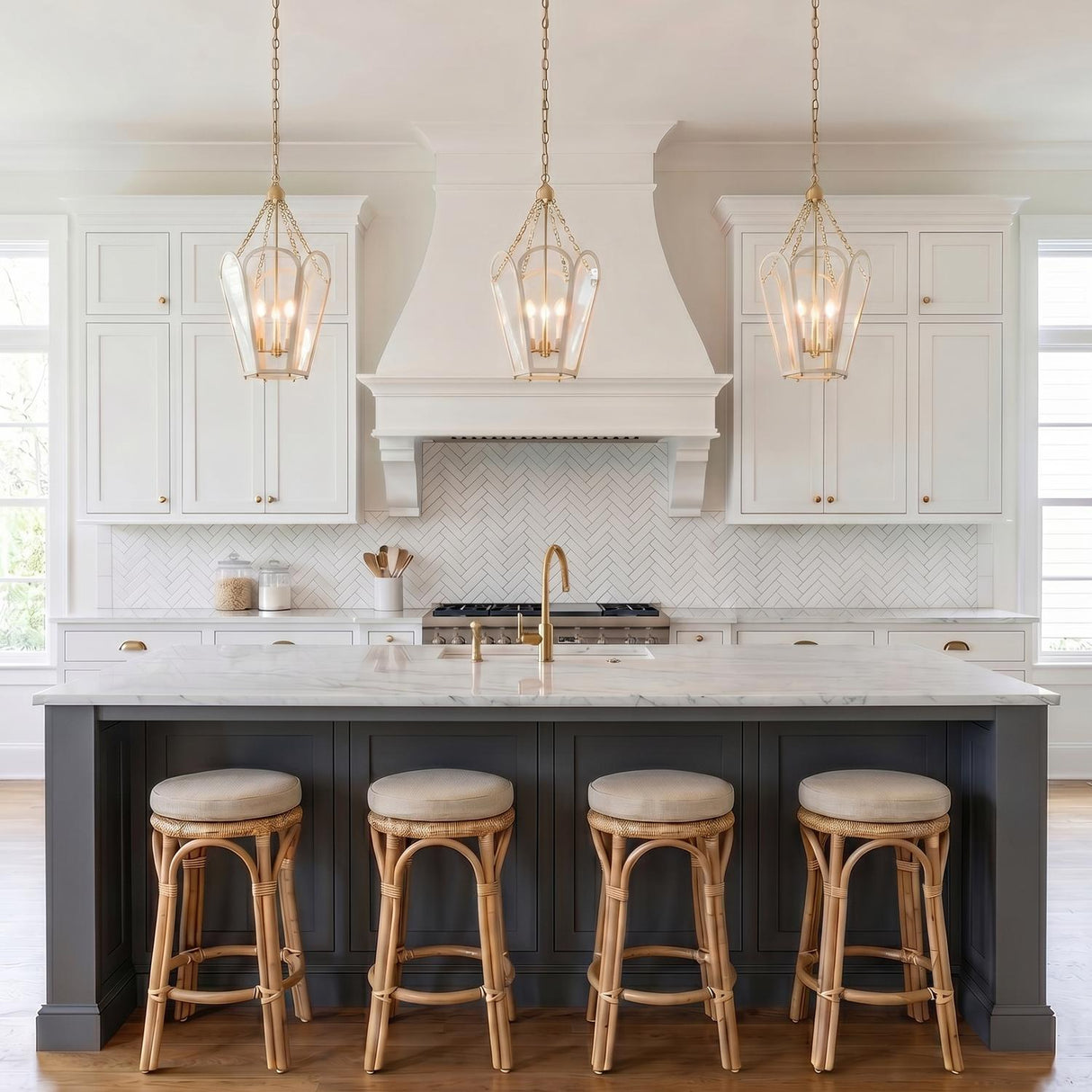 A transitional kitchen with three Ravenna Medium Pendants in cream and aged brass over a marble island with a gray base and four rattan bar stools.