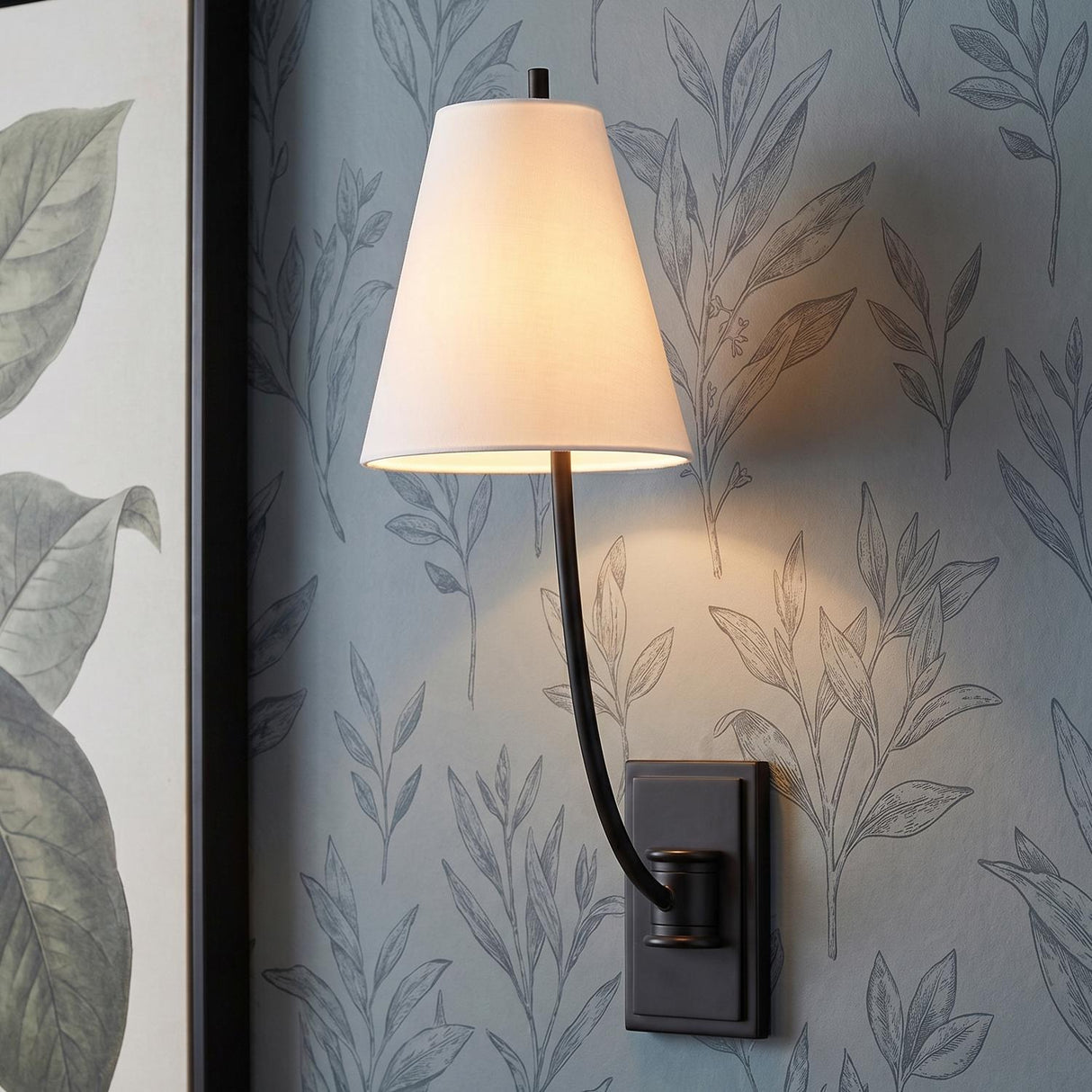 Cordelia Wall Sconce 18", Aged Iron linear curved arm Wall Sconce in a Transitional Bedroom with botanical wallpaper and framed art.