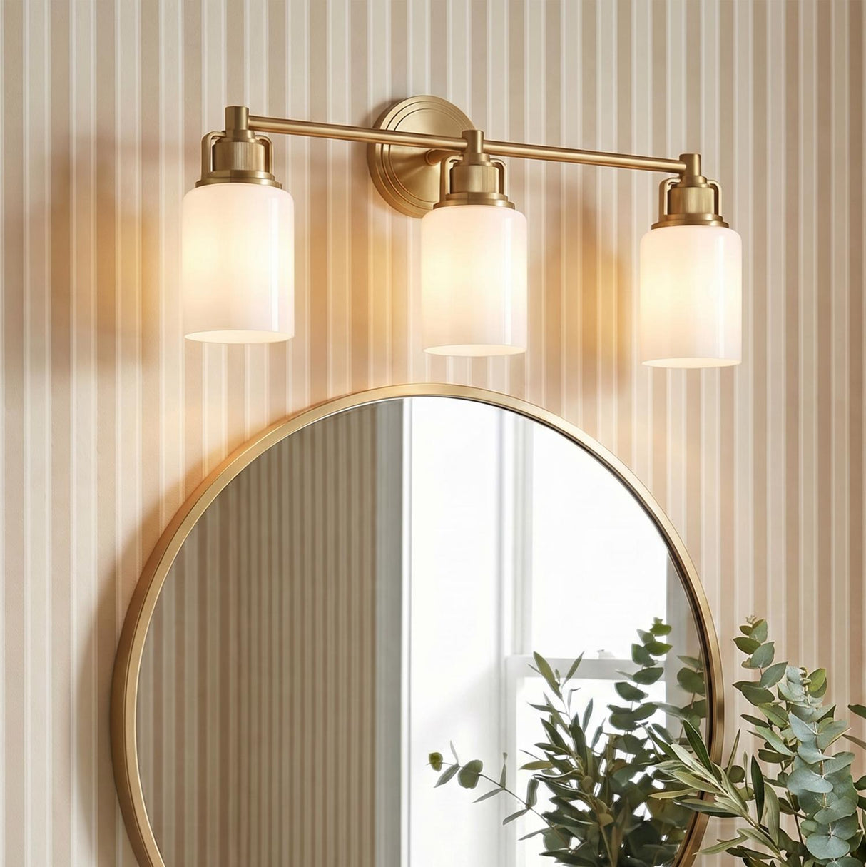 Claxton 3 Light Vanity 24", Modern Brass linear vanity in a Transitional Bathroom with a round brass mirror and striped wallpaper.