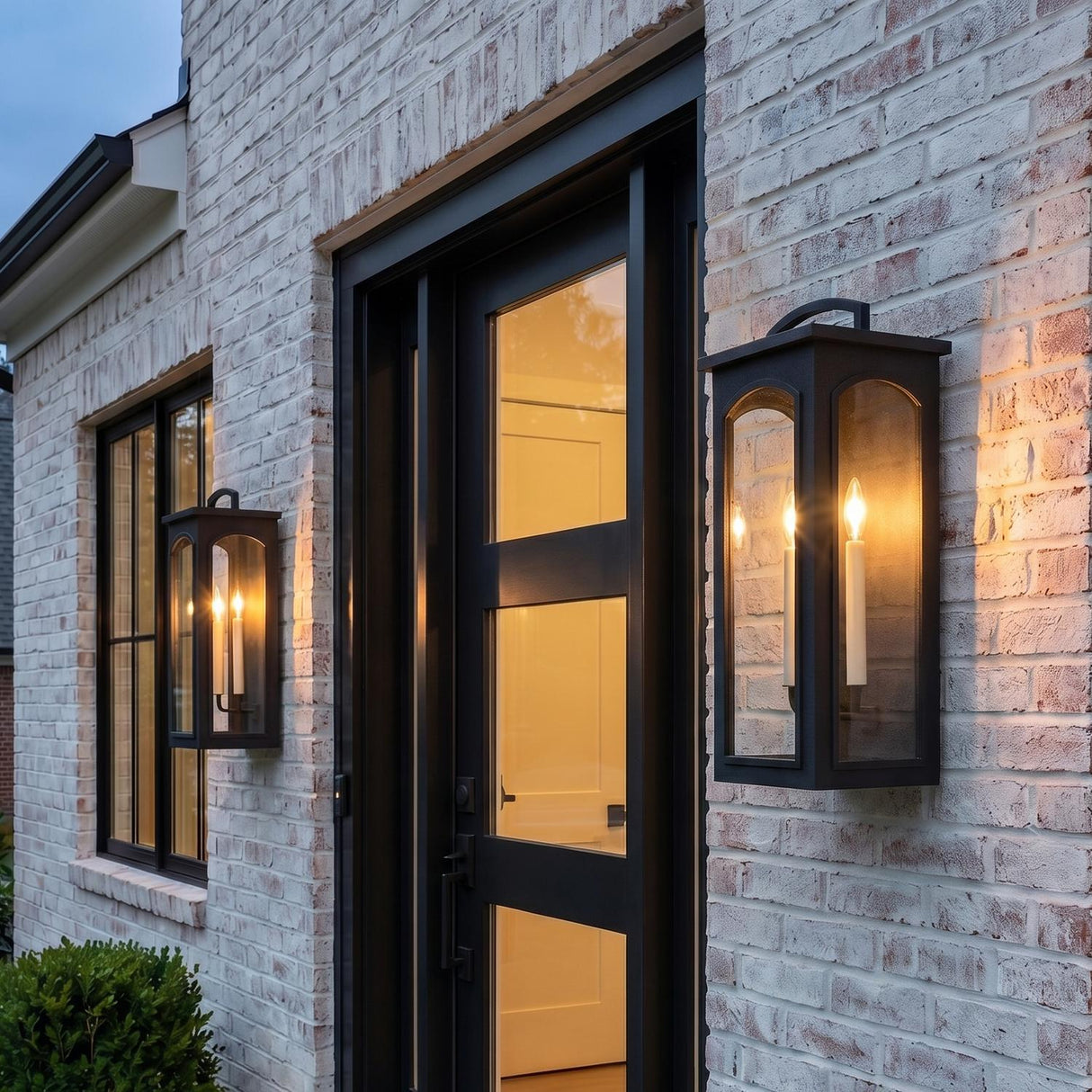 A modern farmhouse entryway featuring two Barlow Outdoor Wall Light lanterns in textured black flanking a black front door on a whitewashed brick exterior.