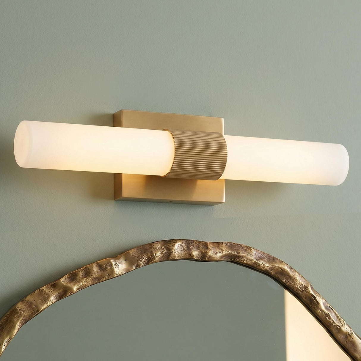 A modern bathroom featuring a Ramsey LED Vanity Light 18 inch in satin brass with a frosted glass tube mounted above a hammered gold mirror.
