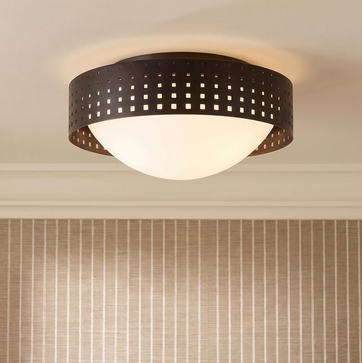A transitional foyer with an Egan Medium Flush Mount featuring an Urban Bronze perforated band and frosted glass dome above striped beige wallpaper and white crown molding.