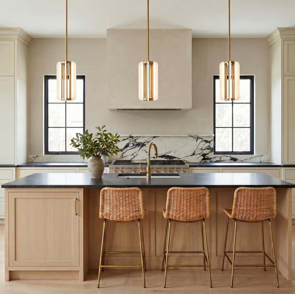 A modern farmhouse kitchen with three vintage brass Dagan LED Pendants over a light wood island with woven rattan stools and a marble backsplash.