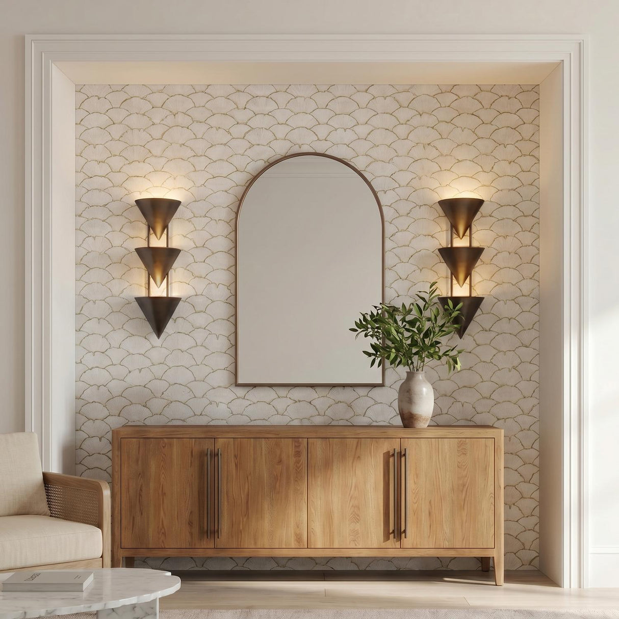 A transitional foyer with two Zora 3 Light Wall Sconces in aged steel flanking an arched mirror above a light wood sideboard and scalloped wallpaper.