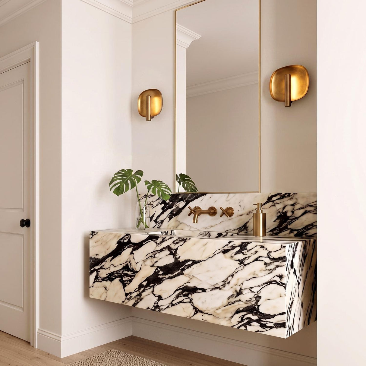A contemporary bathroom with two Orlene LED Wall Sconce 8", Vintage Brass fixtures flanking a mirror above a floating black and white veined marble vanity.