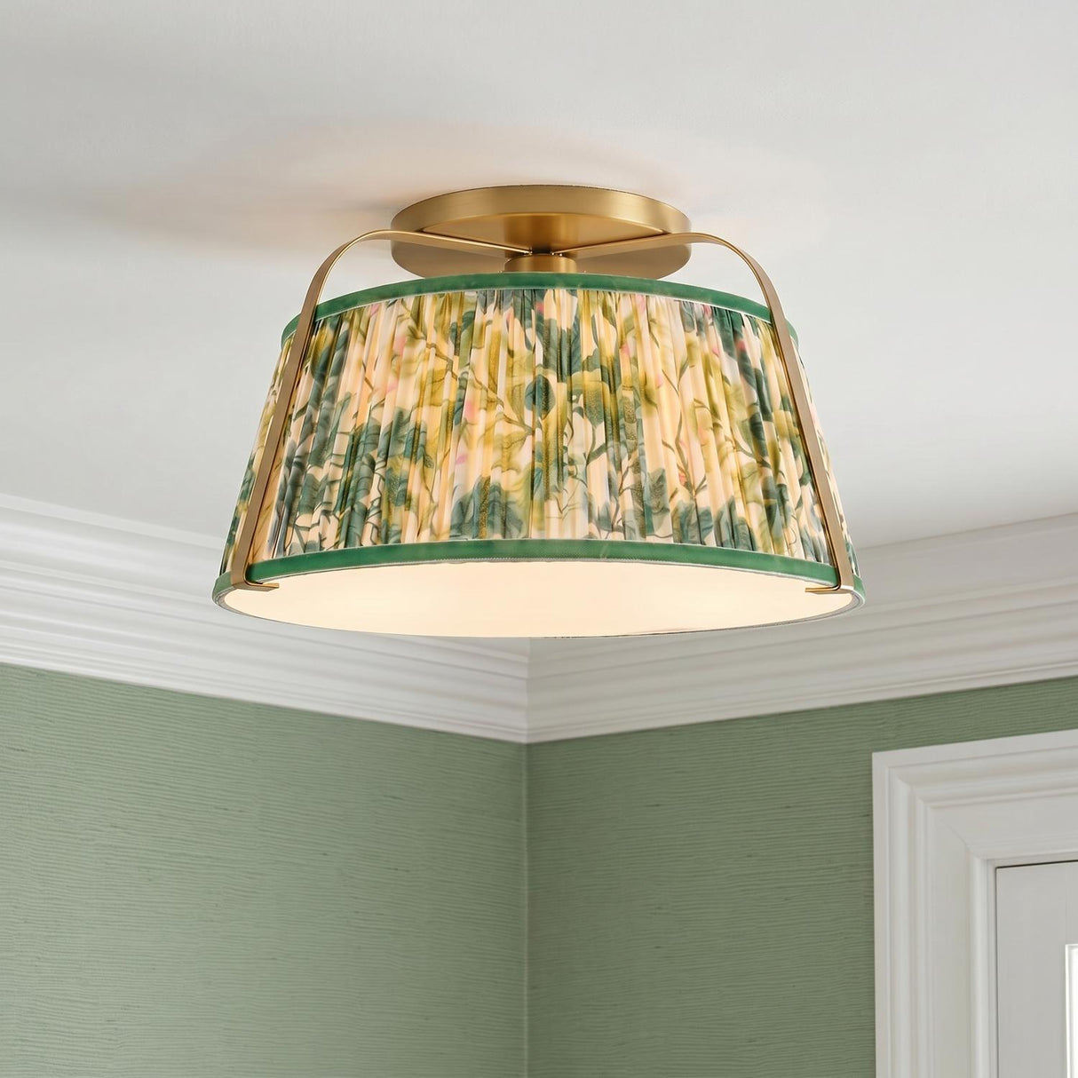 A traditional bedroom with a brushed brass and green floral fabric semi-flush mount installed on a standard ceiling above green grasscloth wallpaper and white crown molding.