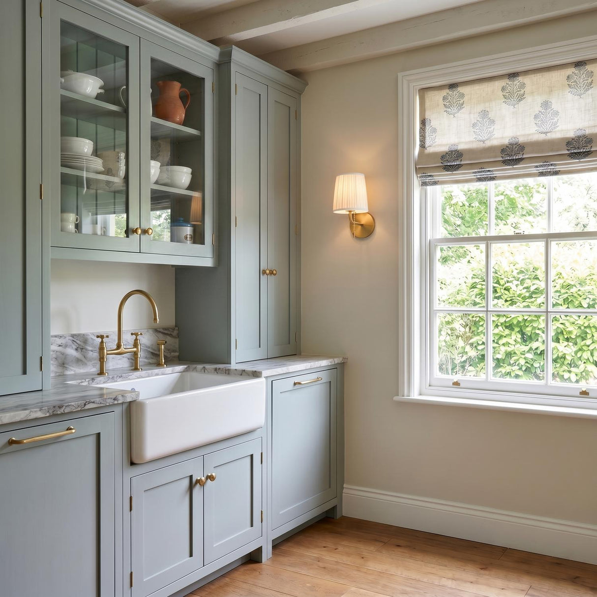 A modern farmhouse kitchen with a Daina Wall Sconce 10", Brushed Brass and White featuring a linen shade mounted beside sage green cabinets under a beamed ceiling.