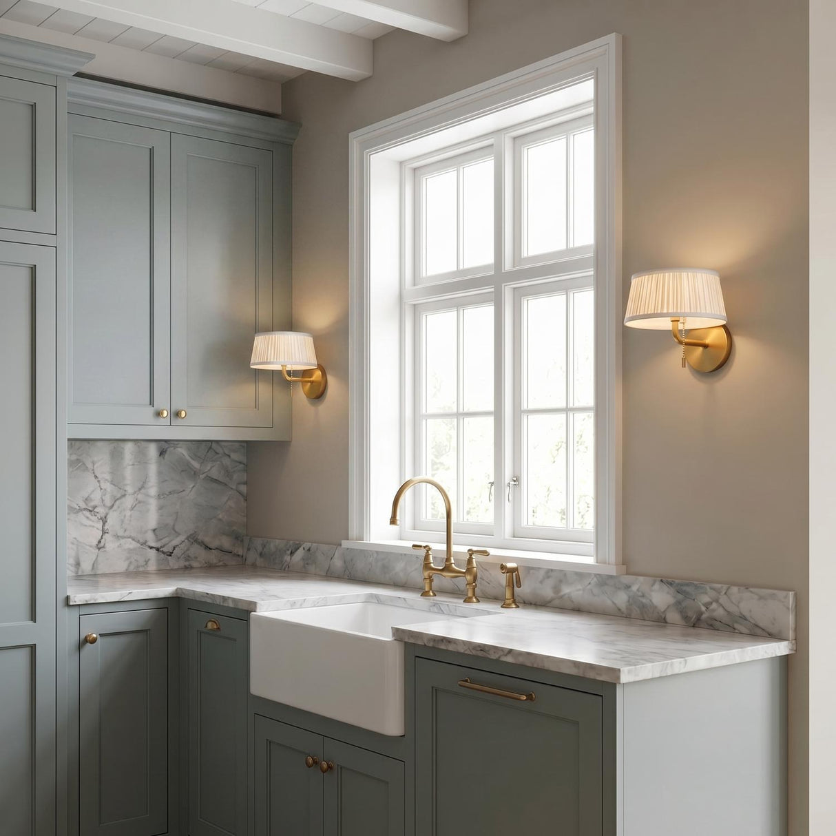 A transitional kitchen with a beamed ceiling and two Daina Wall Sconces in brushed brass and white flanking a window over a marble countertop and apron sink.