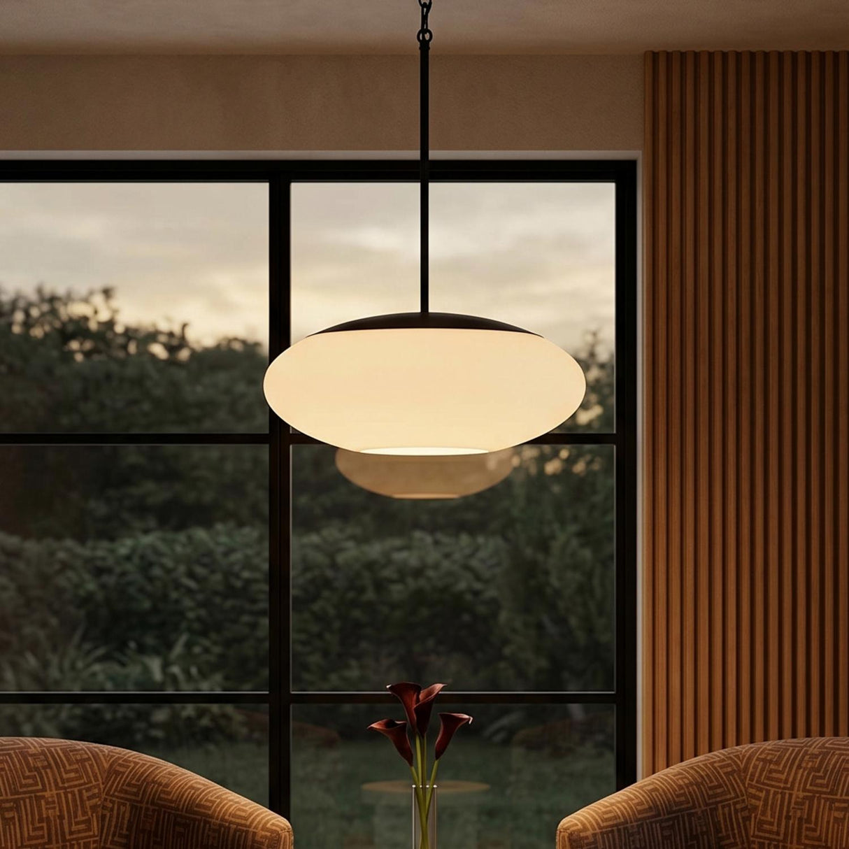 A mid-century living room with the Evora Pendant in Matte Black and Opal Glass suspended from the ceiling center near fluted wood paneling and a large window.