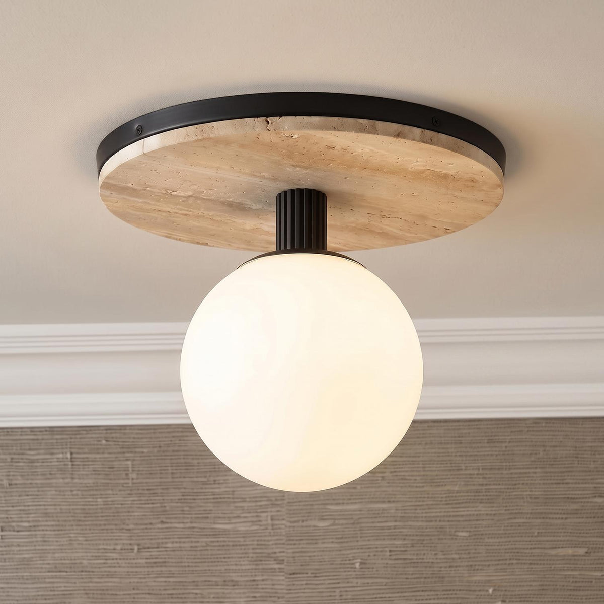 A modern foyer features a matte black Araceli flush mount with a white glass globe and travertine base mounted to the ceiling above textured tan grasscloth wallpaper.