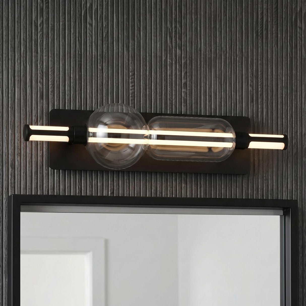 A modern bathroom featuring a Latimer LED Vanity Light 26" in matte black and clear glass mounted above a mirror on a dark grey slat wall.