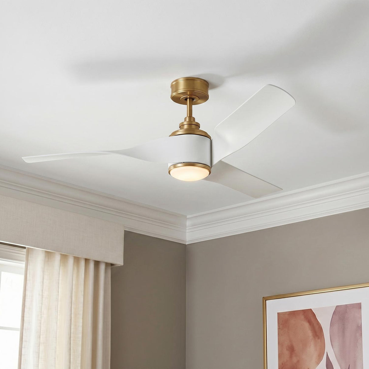 A contemporary bedroom with the Merlin LED Ceiling Fan 60-inch in matte white and modern brass mounted above taupe walls and framed abstract wall art.