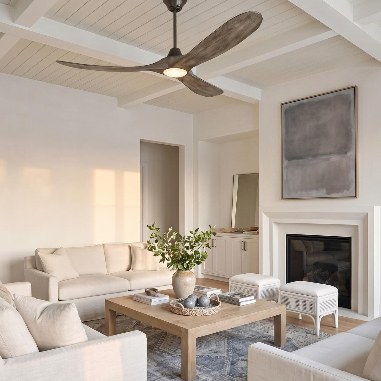 A modern living room with the Egret LED Ceiling Fan 60 in gray wash oak and aged pewter on a beamed ceiling above white sofas and a fireplace.