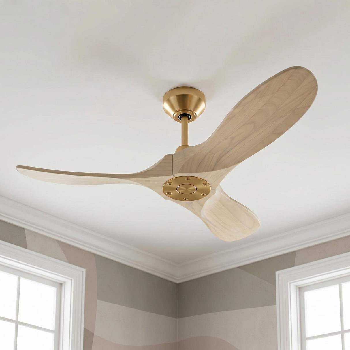A modern bedroom with an Egret Ceiling Fan in whitewash oak and modern brass finishes mounted on a standard ceiling above neutral patterned wallpaper and white windows.