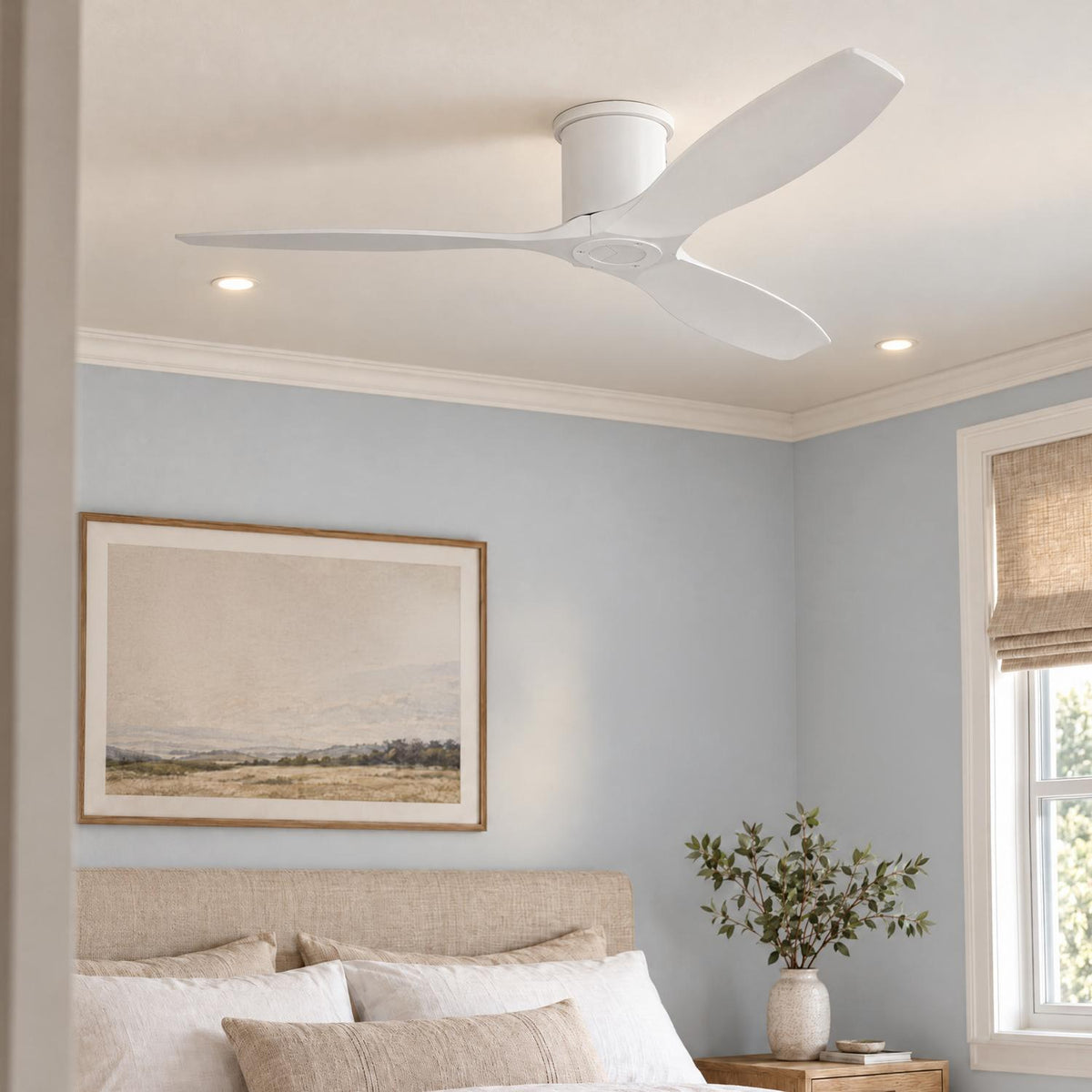 A coastal bedroom features a matte white ceiling fan centered above a beige upholstered headboard, light blue walls, and a woven window shade.