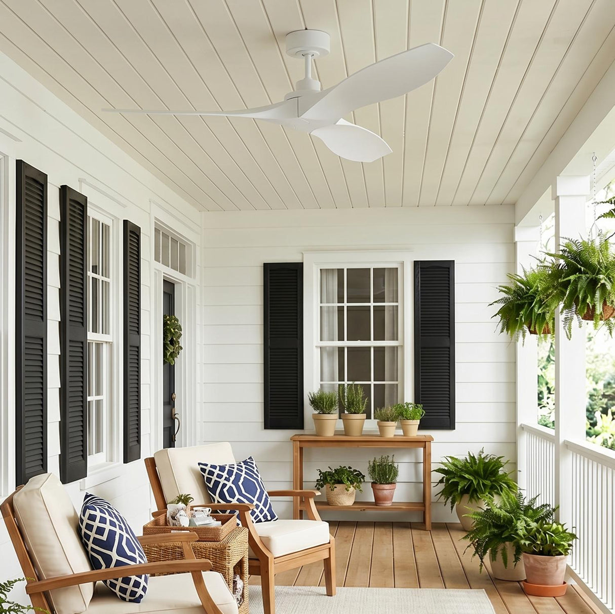 A modern farmhouse porch with white siding and black shutters featuring the matte white Heron Outdoor Smart Ceiling Fan 52 inch above wooden armchairs and potted ferns.