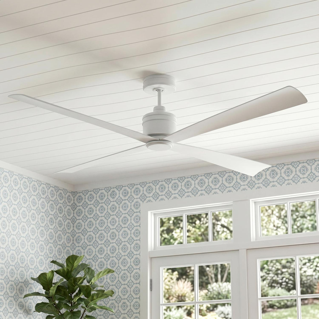 A modern farmhouse living room with the matte white Sora Ceiling Fan 72" mounted to a white shiplap ceiling above blue patterned wallpaper and large windows.