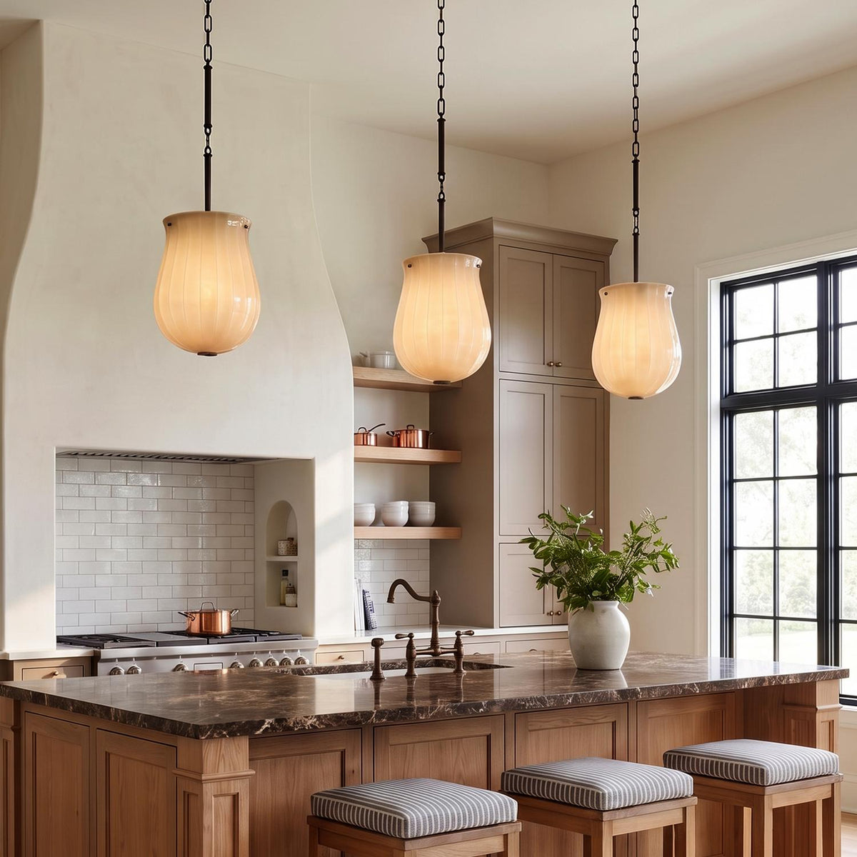 A modern farmhouse kitchen with three Cortland Medium Pendants in champagne glass and distressed bronze hanging over a brown marble island with a white plaster range hood.