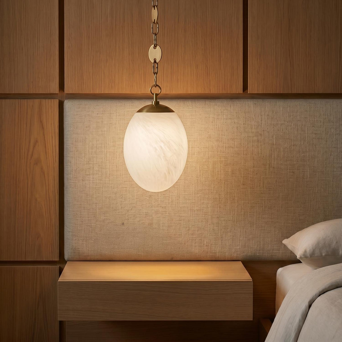 A modern bedroom featuring the Kelton Small Pendant 8", Cloud Glass and Aged Brass hanging over a floating wood nightstand beside a linen textured headboard.