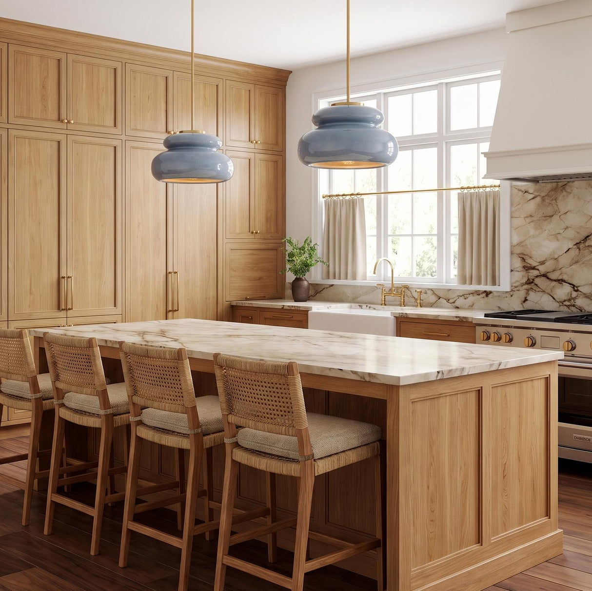 A transitional kitchen features two Ellsworth Pendants in blue crackle ceramic and aged brass hanging over a white marble island surrounded by natural wood cabinetry.