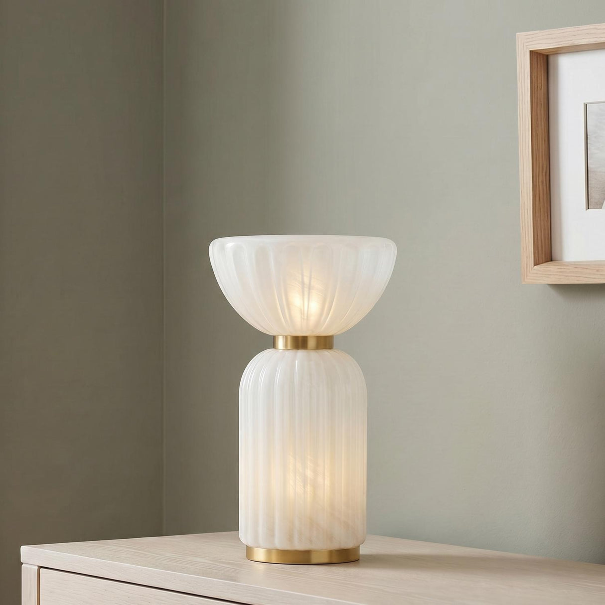A contemporary living room featuring the Dorset Table Lamp 17", Fluted Cloud Glass and Aged Brass on a light wood dresser beside a natural wood frame.