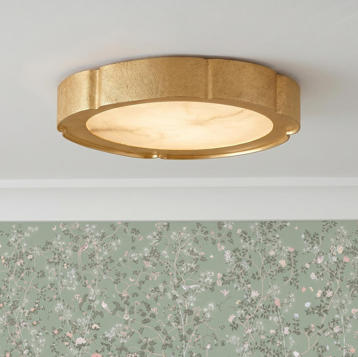 A traditional foyer with a gold leaf and alabaster flush mount on a white ceiling above sage green floral wallpaper and white crown molding.