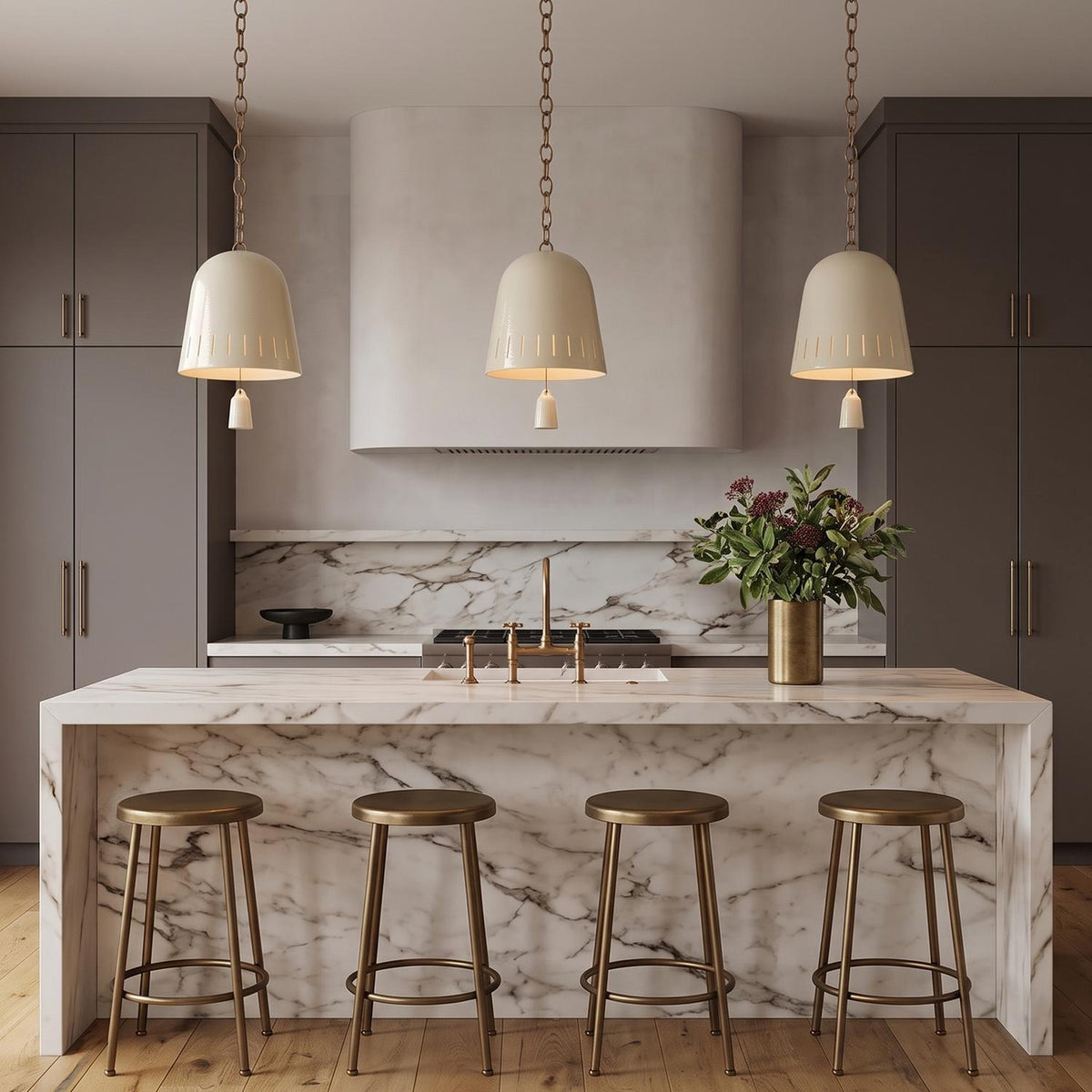 A transitional kitchen with three Briony Medium Pendants in ivory glaze and patina brass suspended over a white marble waterfall island and dark gray cabinetry.