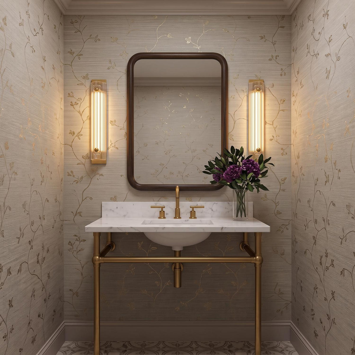 A transitional bathroom with two gold leaf and reeded glass wall sconces flanking a dark wood mirror above a marble console vanity with tan floral wallpaper.
