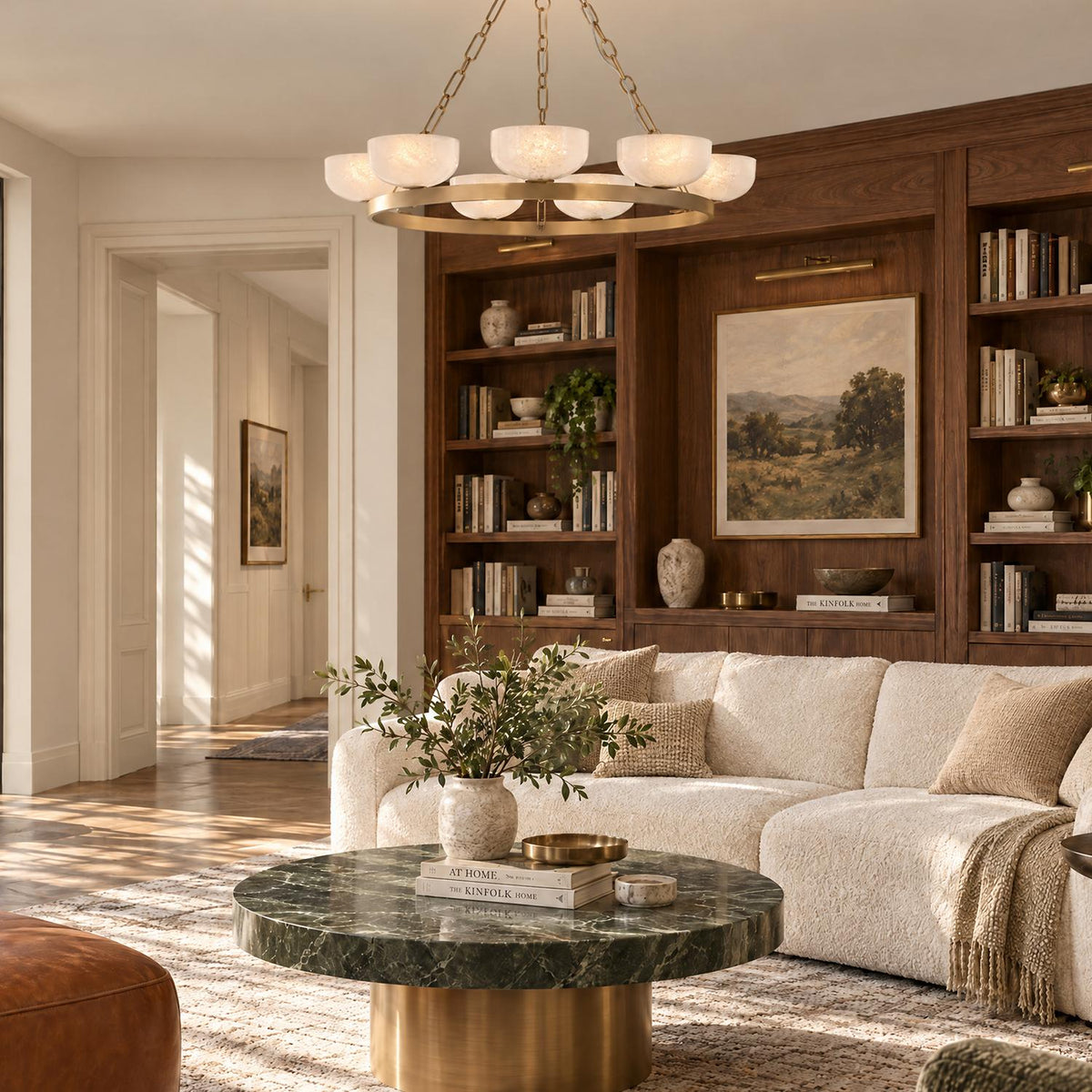 A transitional living room features the Halcyon 9 Light Chandelier 44", Patina Brass and Seeded Cloud Glass suspended above a green marble coffee table.