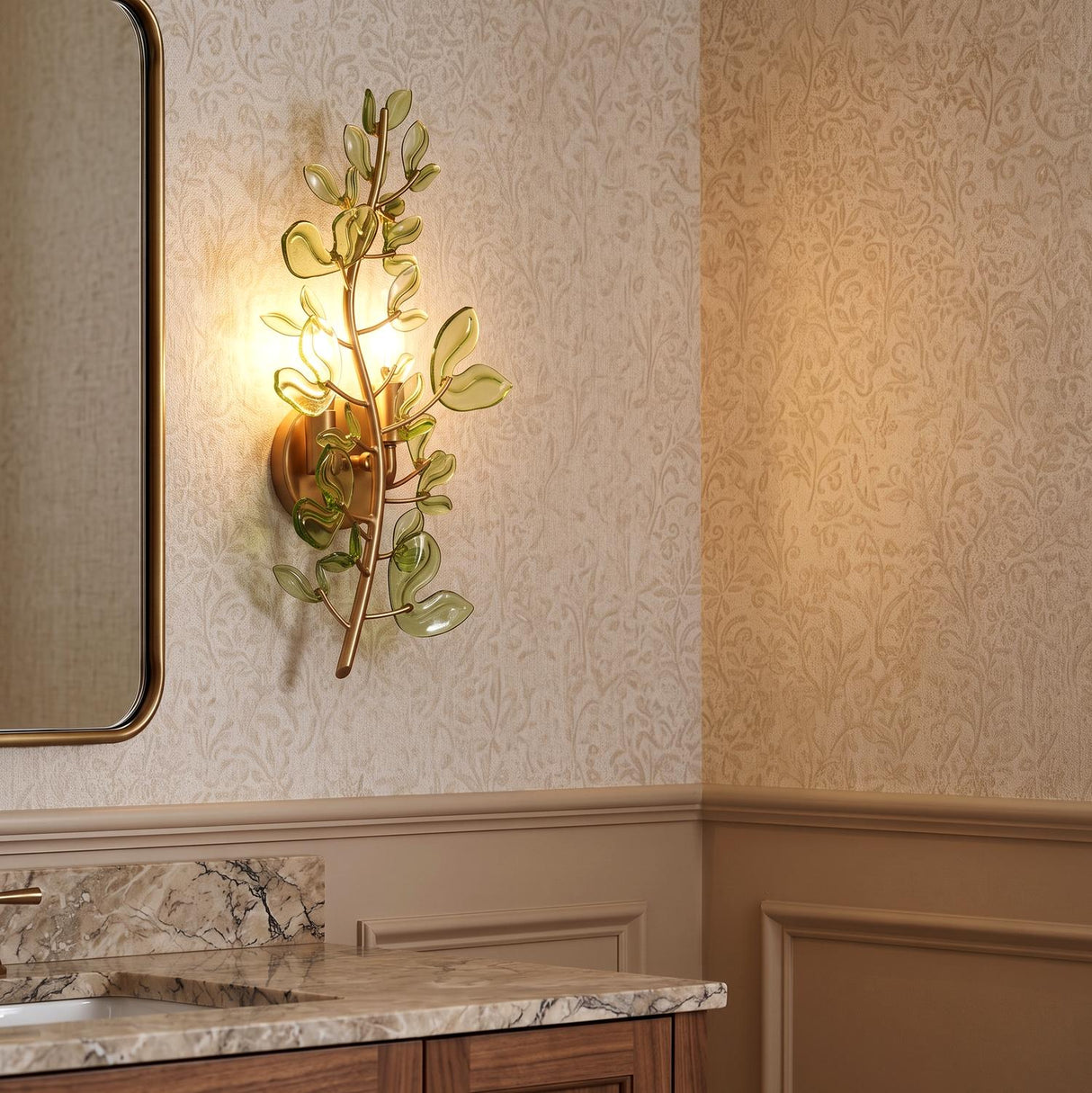 A transitional bathroom with the Esme Wall Sconce 19", Soft Brass and Green Glass mounted on floral wallpaper beside a rounded mirror and marble vanity.