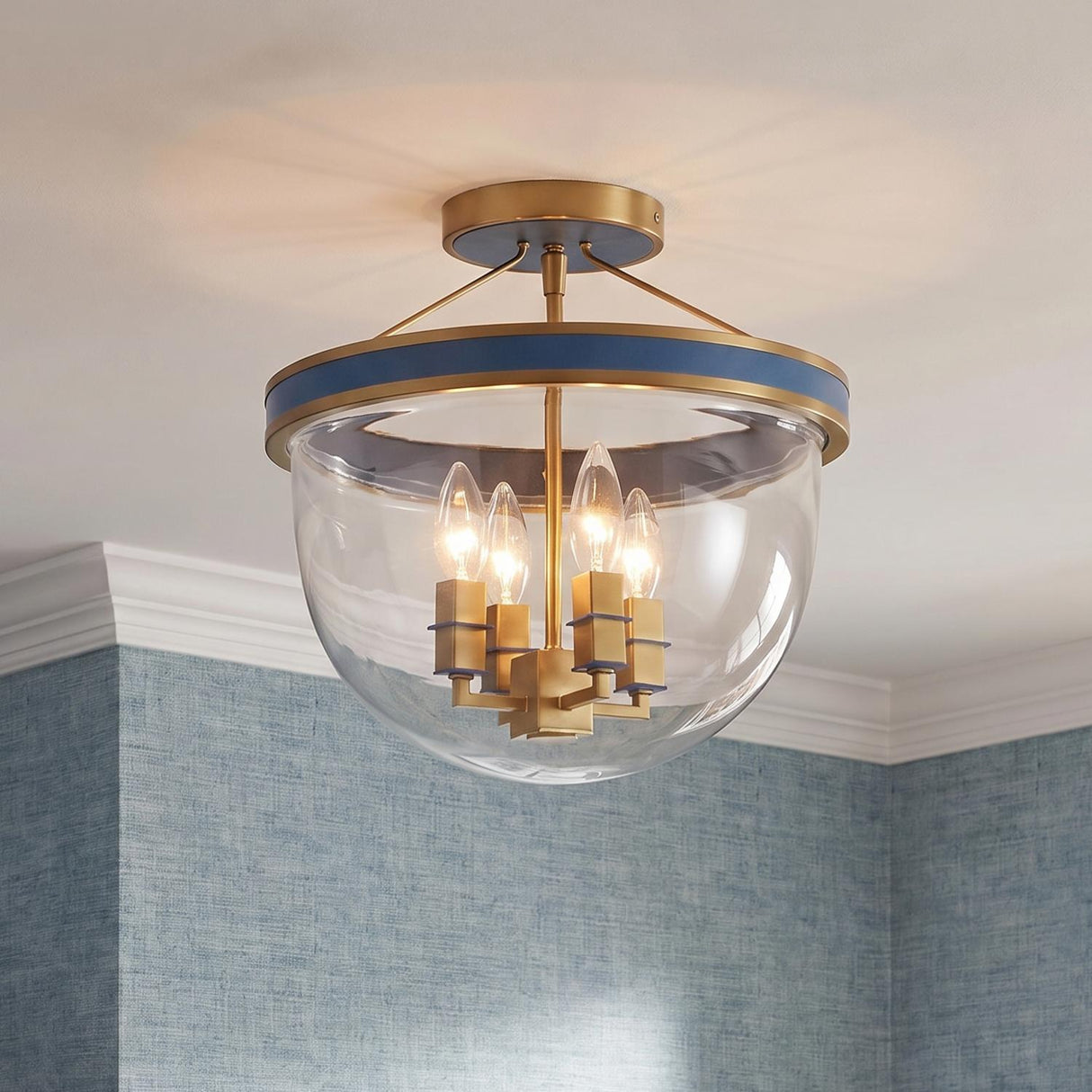 A transitional foyer featuring the Ramona Semi-Flush 13, Brass and Vintage Blue fixture with brushed brass and clear glass set against blue grasscloth wallpaper and white crown molding.