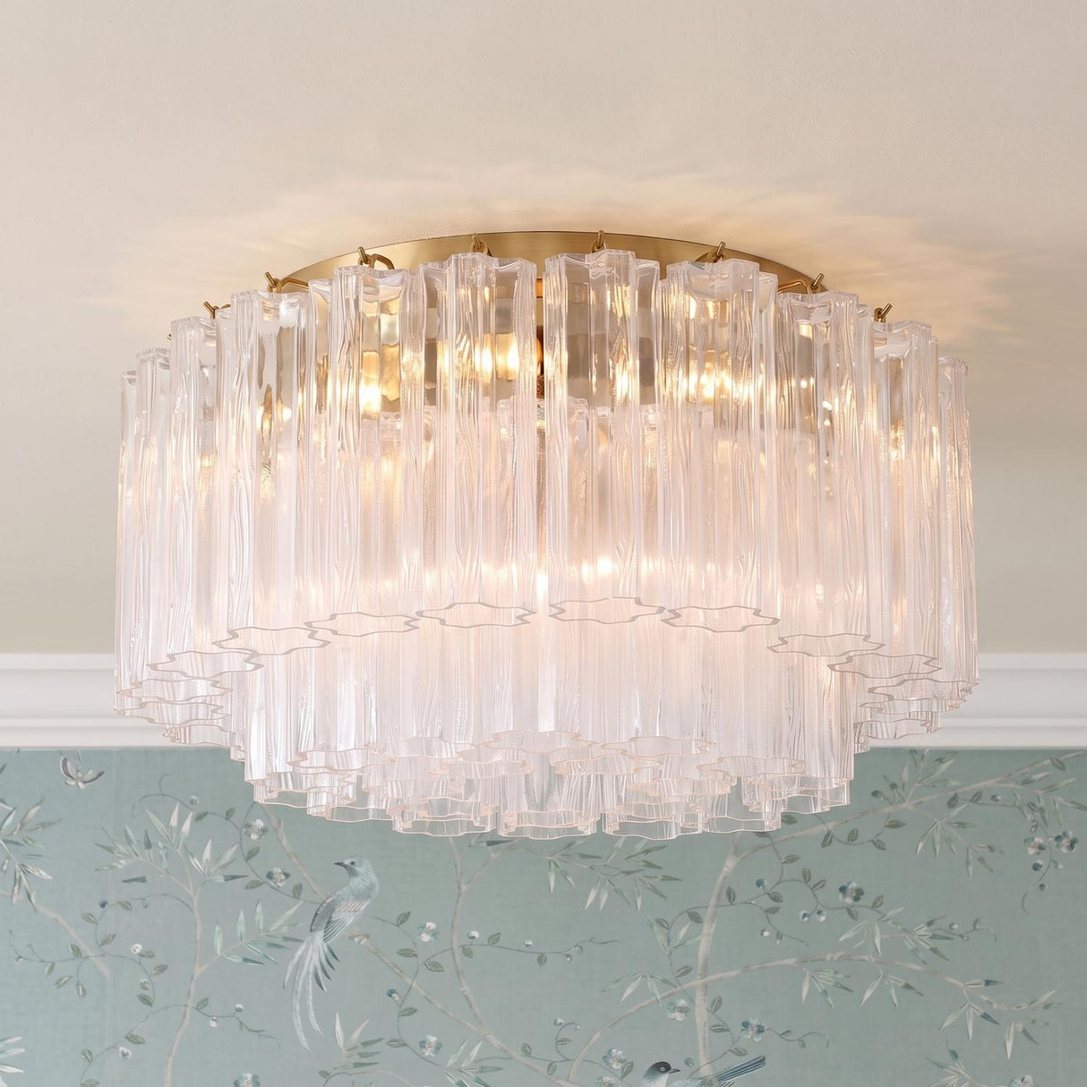 A transitional foyer with the Grace Flush Mount 22", Brass with Clear Glass featuring textured rods along a standard ceiling above blue bird-themed chinoiserie wallpaper.