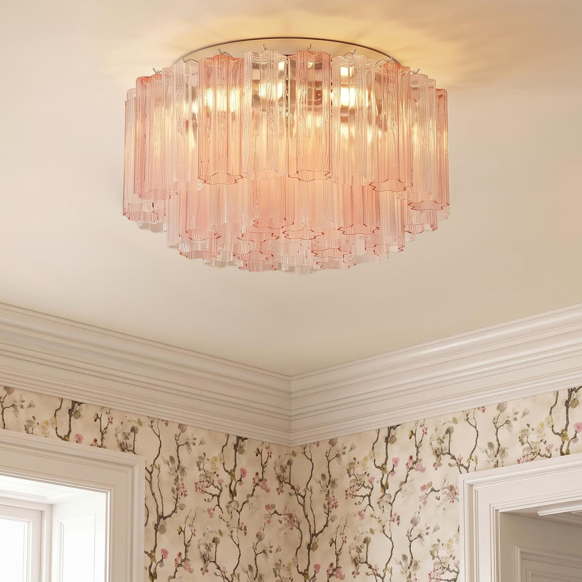A traditional bedroom featuring the Grace Flush Mount 22", Chrome with Blush Glass installed along the ceiling center above floral wallpaper and white crown molding.