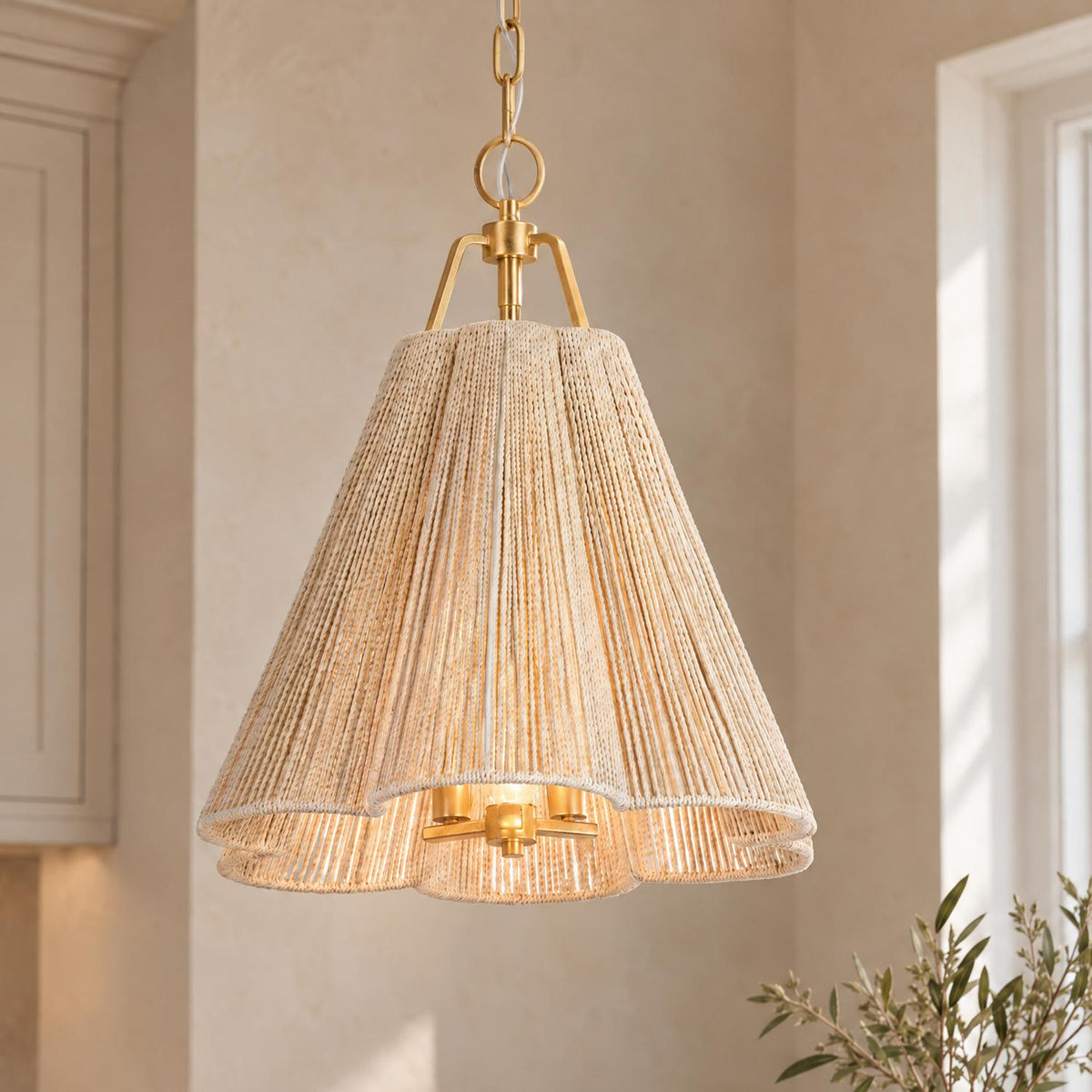 A coastal kitchen featuring the Birdie Medium Pendant in gold leaf and natural rope hanging near off-white shaker cabinets and a bright sunlit window.
