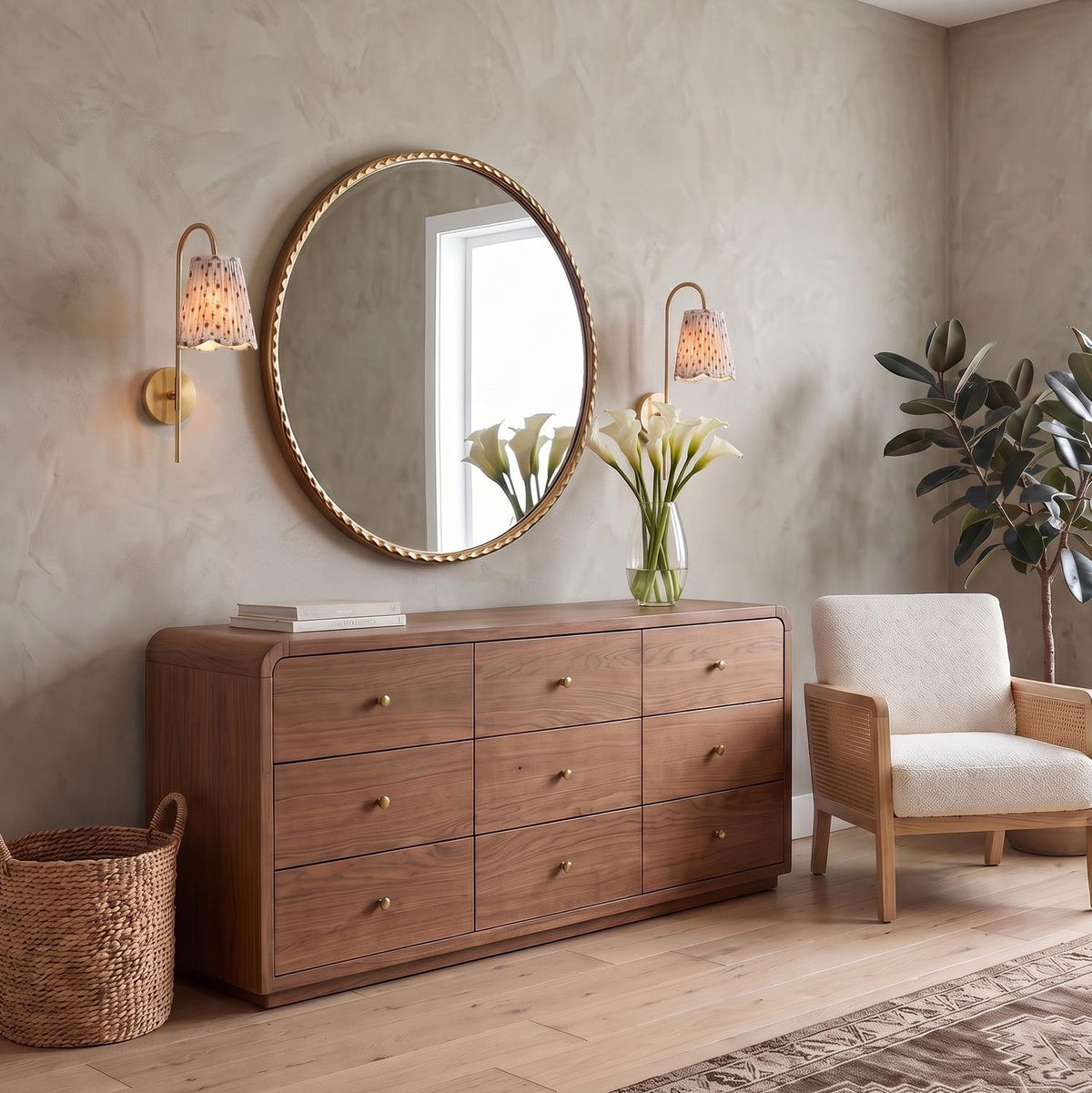 A transitional bedroom featuring the Basil Wall Sconce 19", Aged Brass with Red Primrose Printed Shade flanking a large round mirror above a nine-drawer walnut dresser.