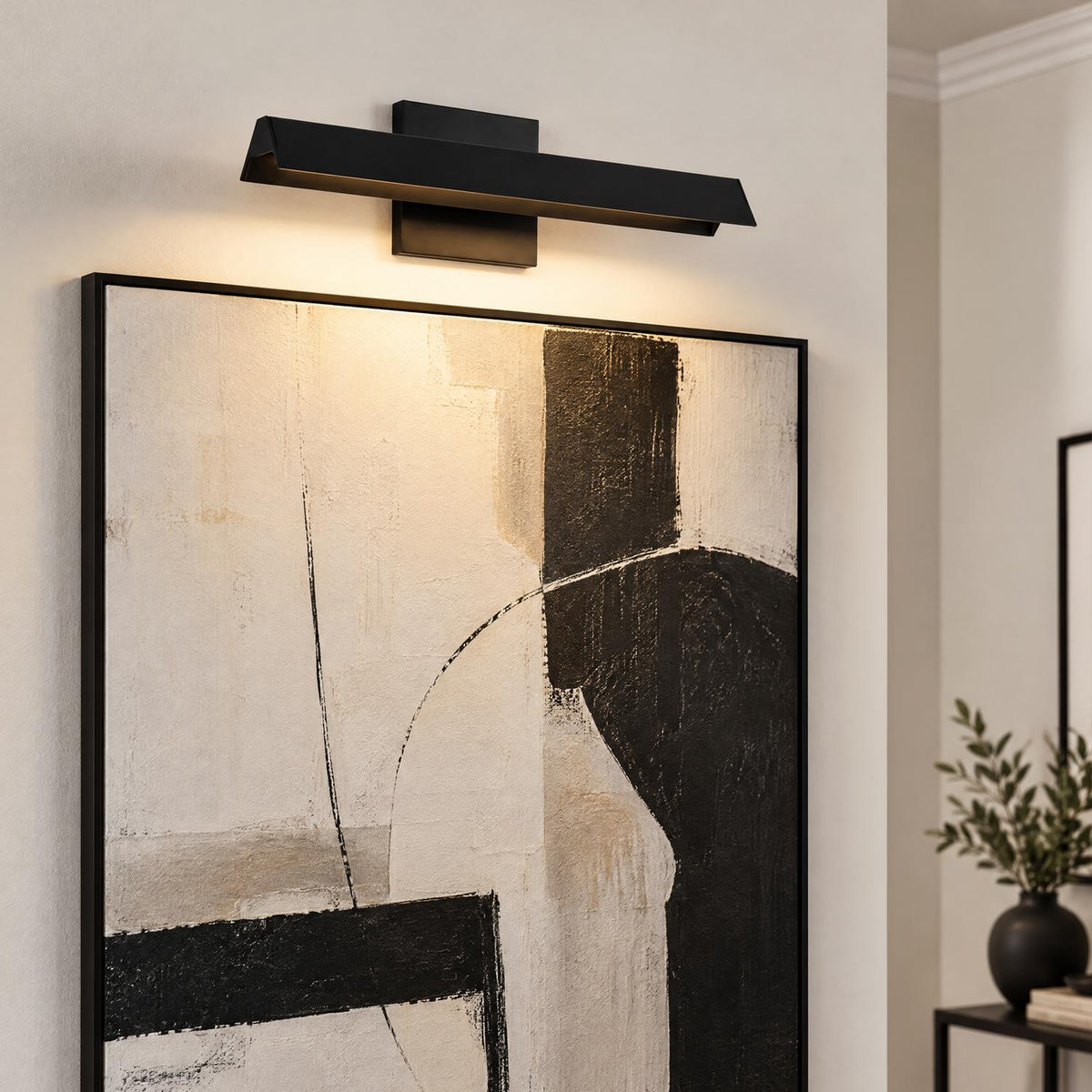 A modern living room features the Avel LED Picture Light 15", Black mounted above a large black and beige abstract canvas artwork.