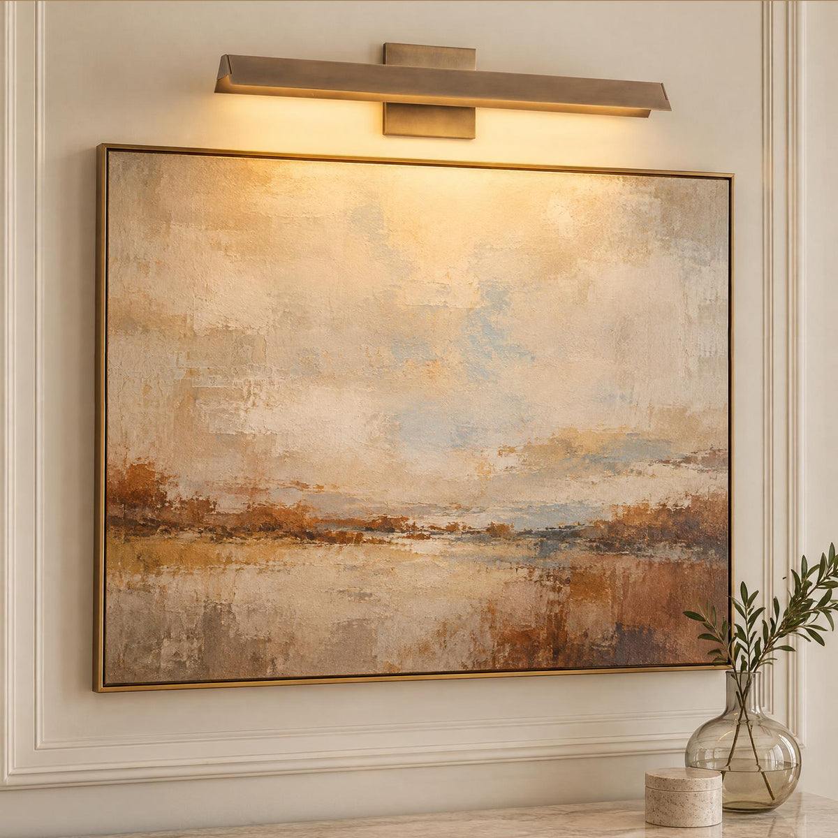 A transitional living room featuring the Avel LED Picture Light 23" in vintage brass mounted above framed abstract wall art and decorative wall molding.
