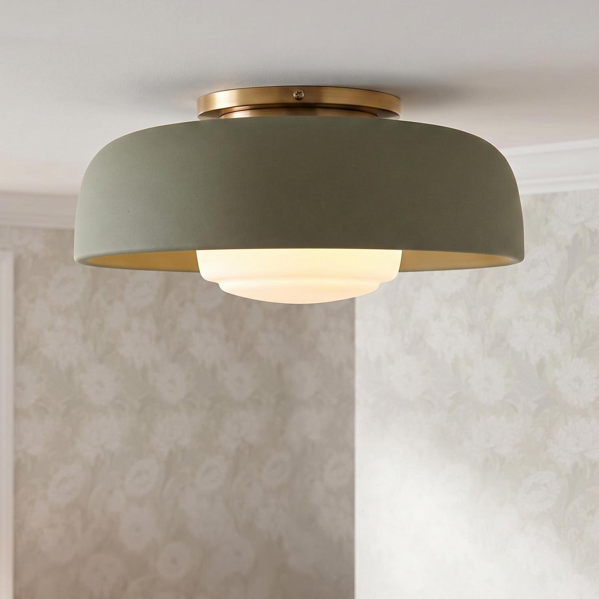 A transitional bedroom featuring the Stratford Medium Flush Mount in aged brass and thyme green mounted to a white ceiling beside neutral floral wallpaper.