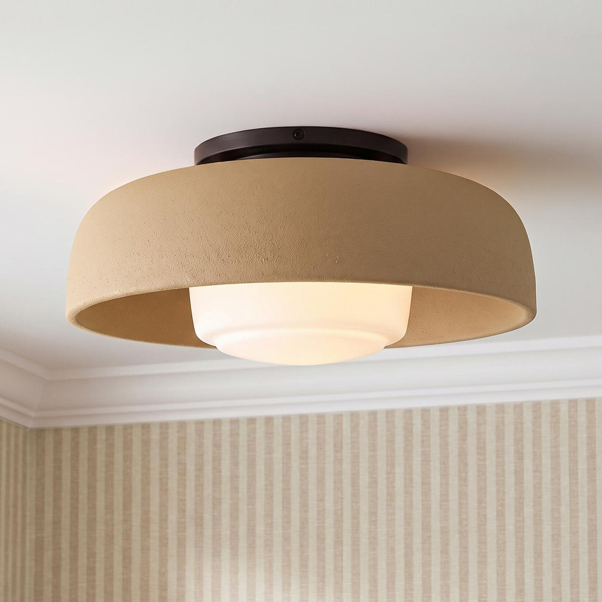 A transitional foyer with the Stratford Medium Flush Mount in aged iron and terracotta finishes mounted along the ceiling above tan striped wallpaper and white crown molding.