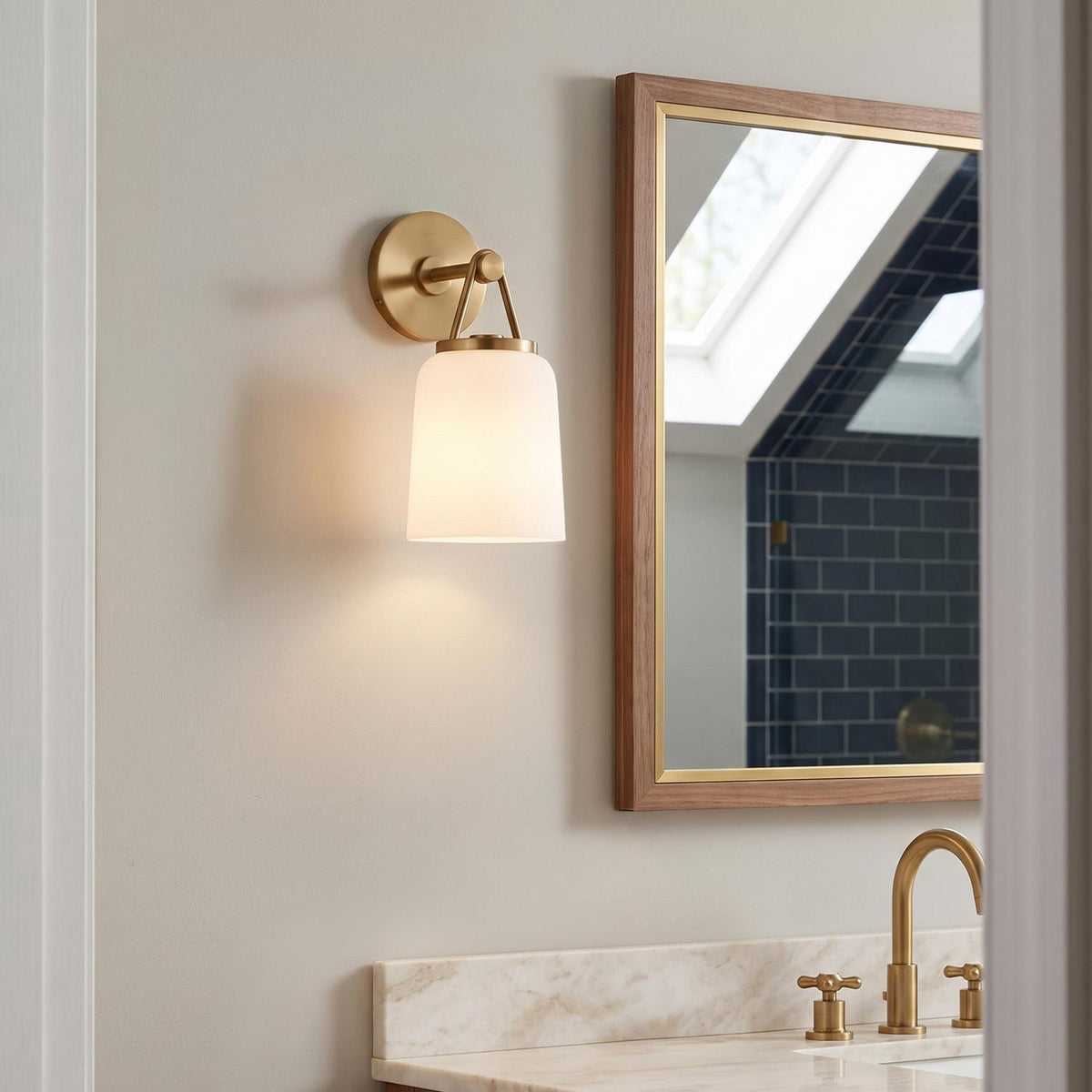 A transitional bathroom with the Stratford Wall Sconce 12", Aged Brass and Opal Glass mounted beside a wood-framed mirror above a marble vanity and navy tile.