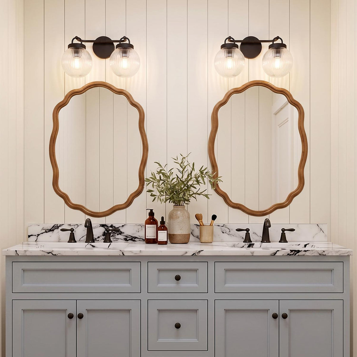 A modern farmhouse bathroom featuring two Whitaker 2 Light Vanity matte black and clear ribbed glass fixtures above scalloped wood mirrors and marble counters.