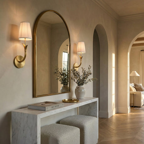 Magnolia Single Wall Sconce 16", Aged Brass finish, shown in a transitional hallway with an arched brass mirror and marble console table.