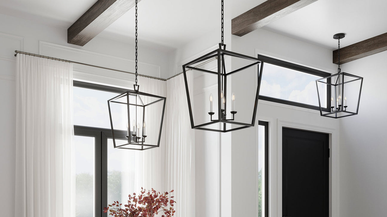 Open Frame Lantern Style Pendants in Matte Black are hung in a lareg room with white walls and wooden exposed beams.